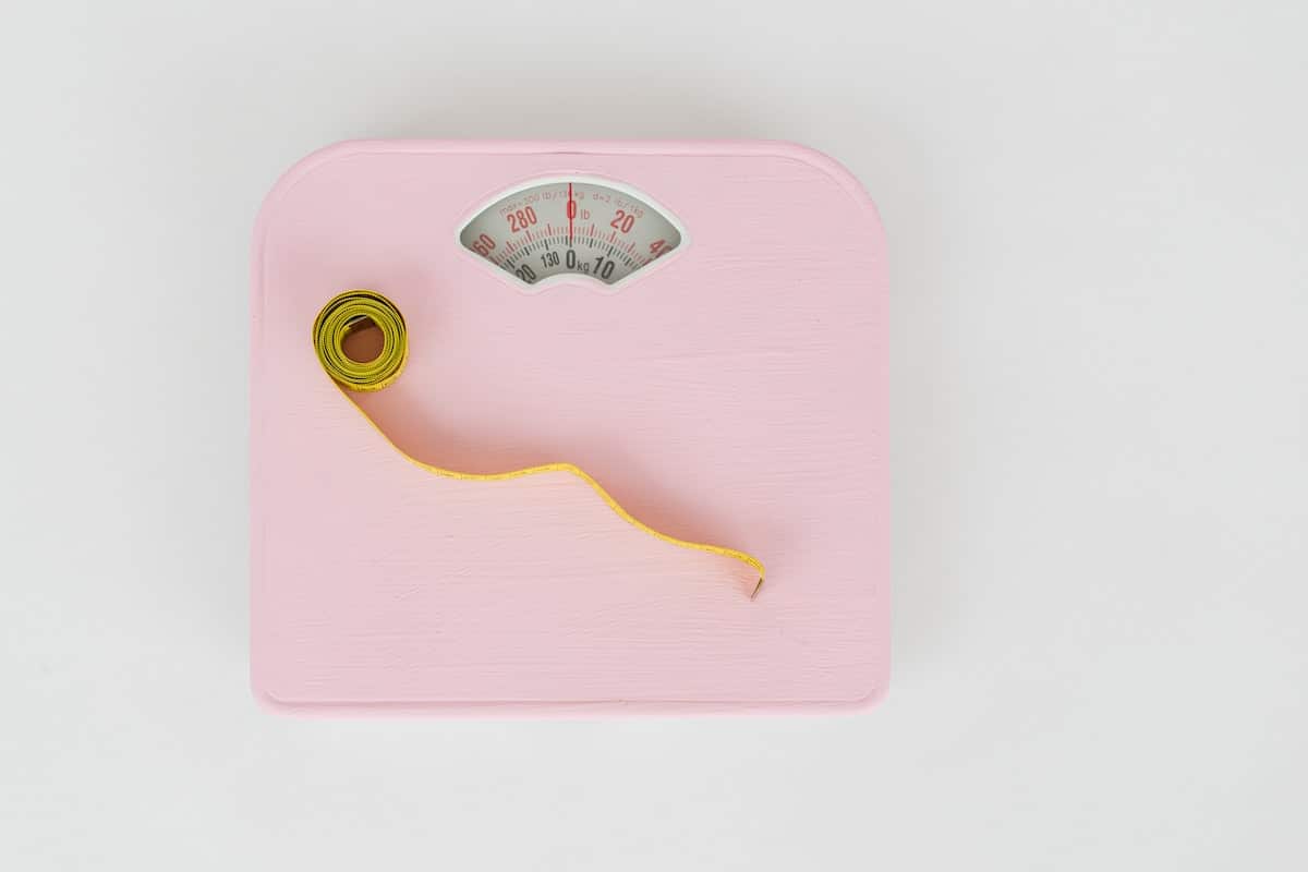 Measure tape with dumbbells and weight scale on the pink