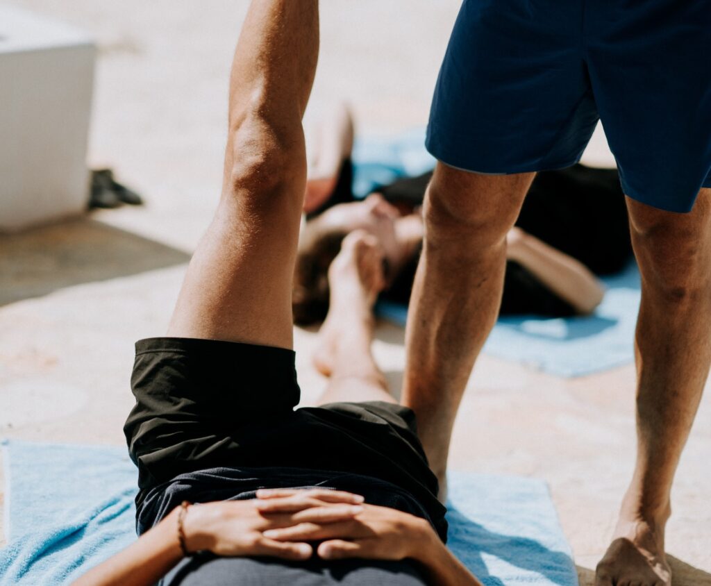 Image of a man holding a person's leg while stretching. Source: Unsplash
