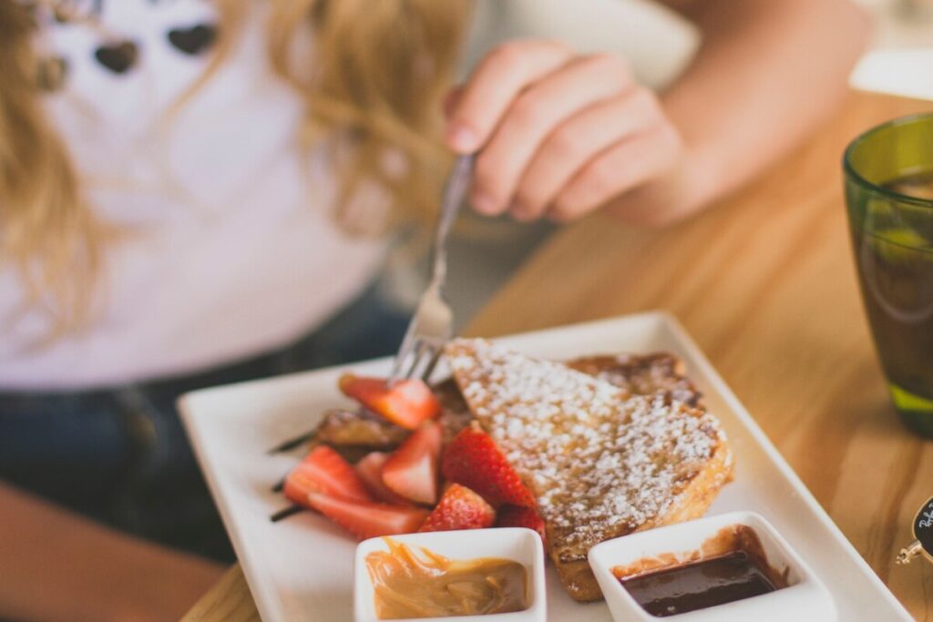 Image of a person with carbohydrate intolerance eating strawberry waffles on a plate. Image source: Unsplash
