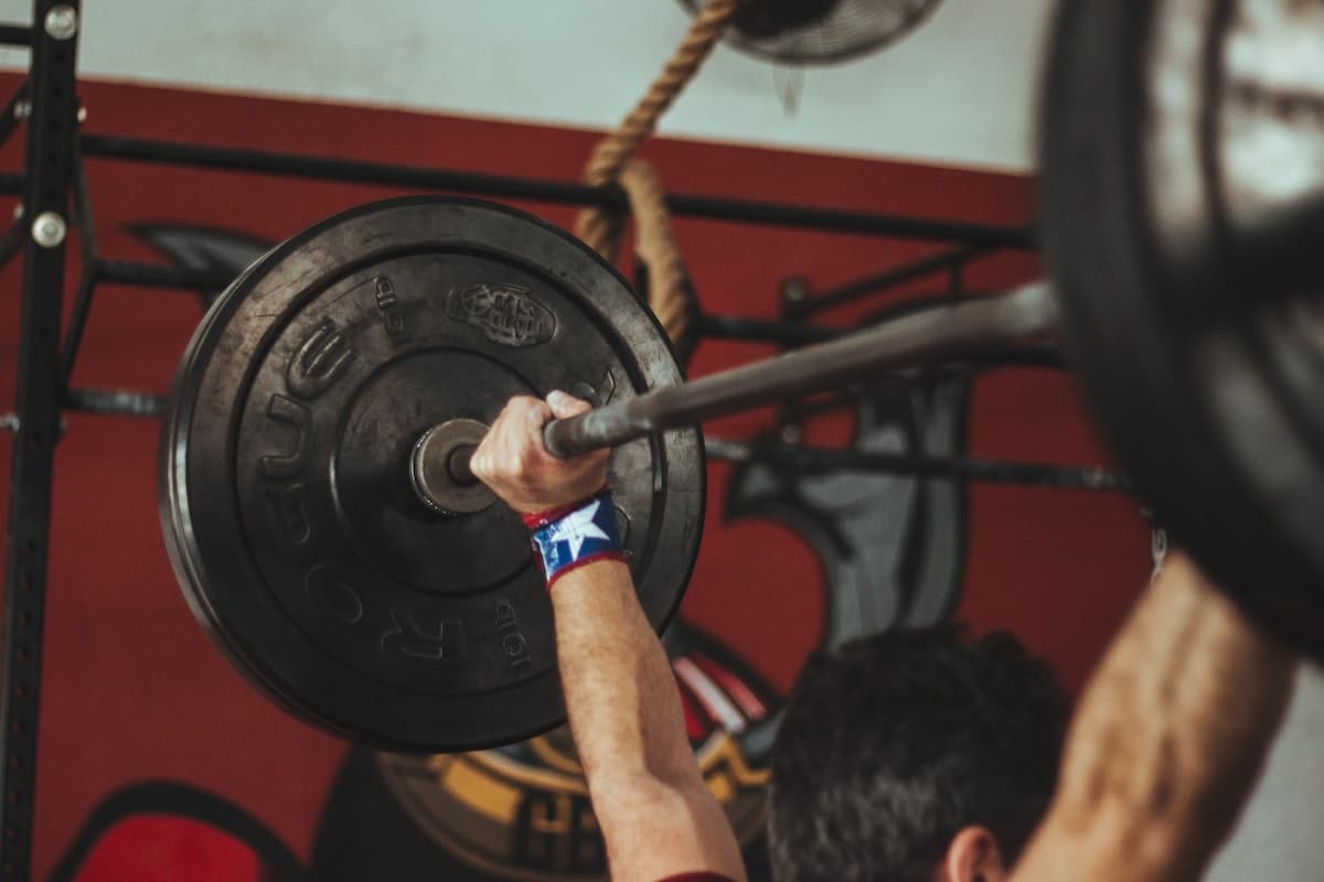 Close up image of a weightlifter lifting a barbell over his head while doing a drop set. Source: Pexels