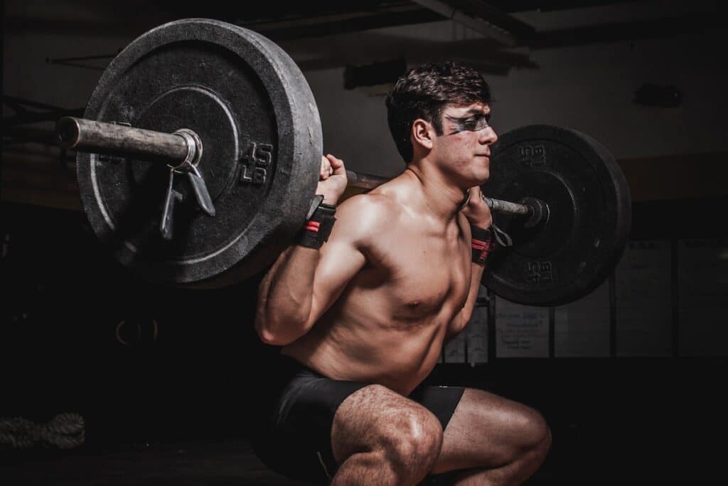 Image of a man doing a back squat with weights. Source: Pexels