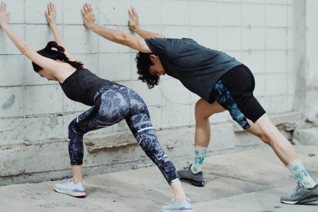 Image of two people doing the soleus stretch on a wall. Source: Pexels