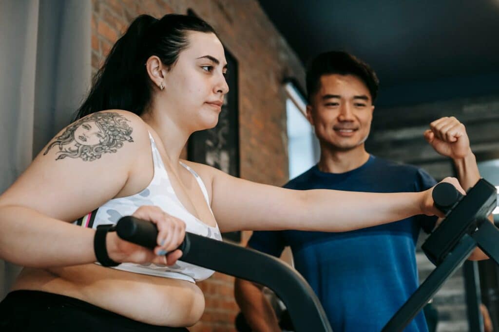 Image of a person  using an elliptical machine with a fitness trainer. Source: Pexels